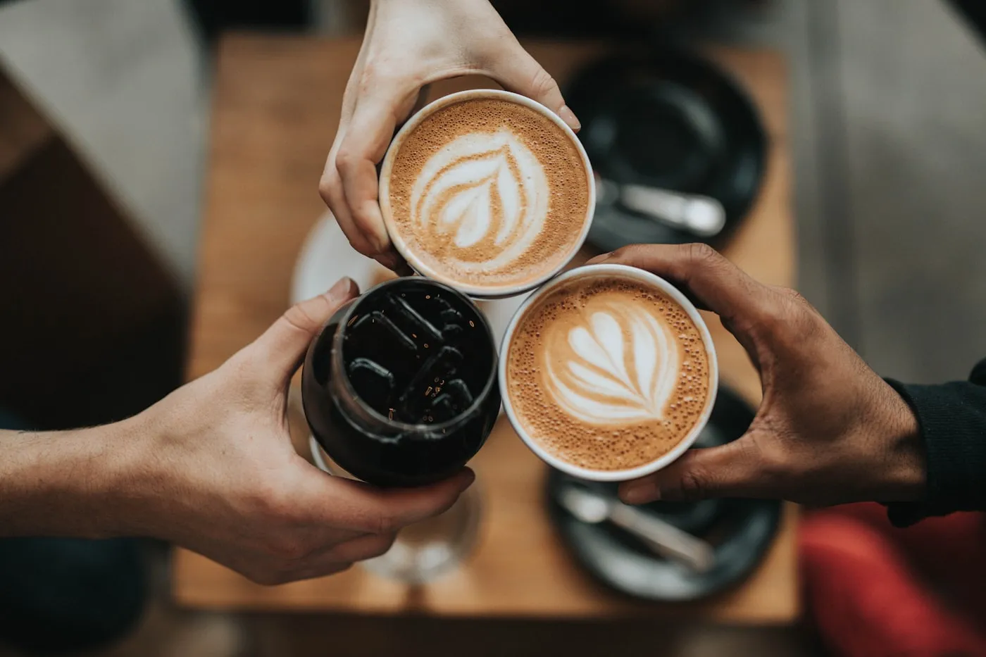 Drei Kaffeetassen werden über einem Tisch zusammengehalten